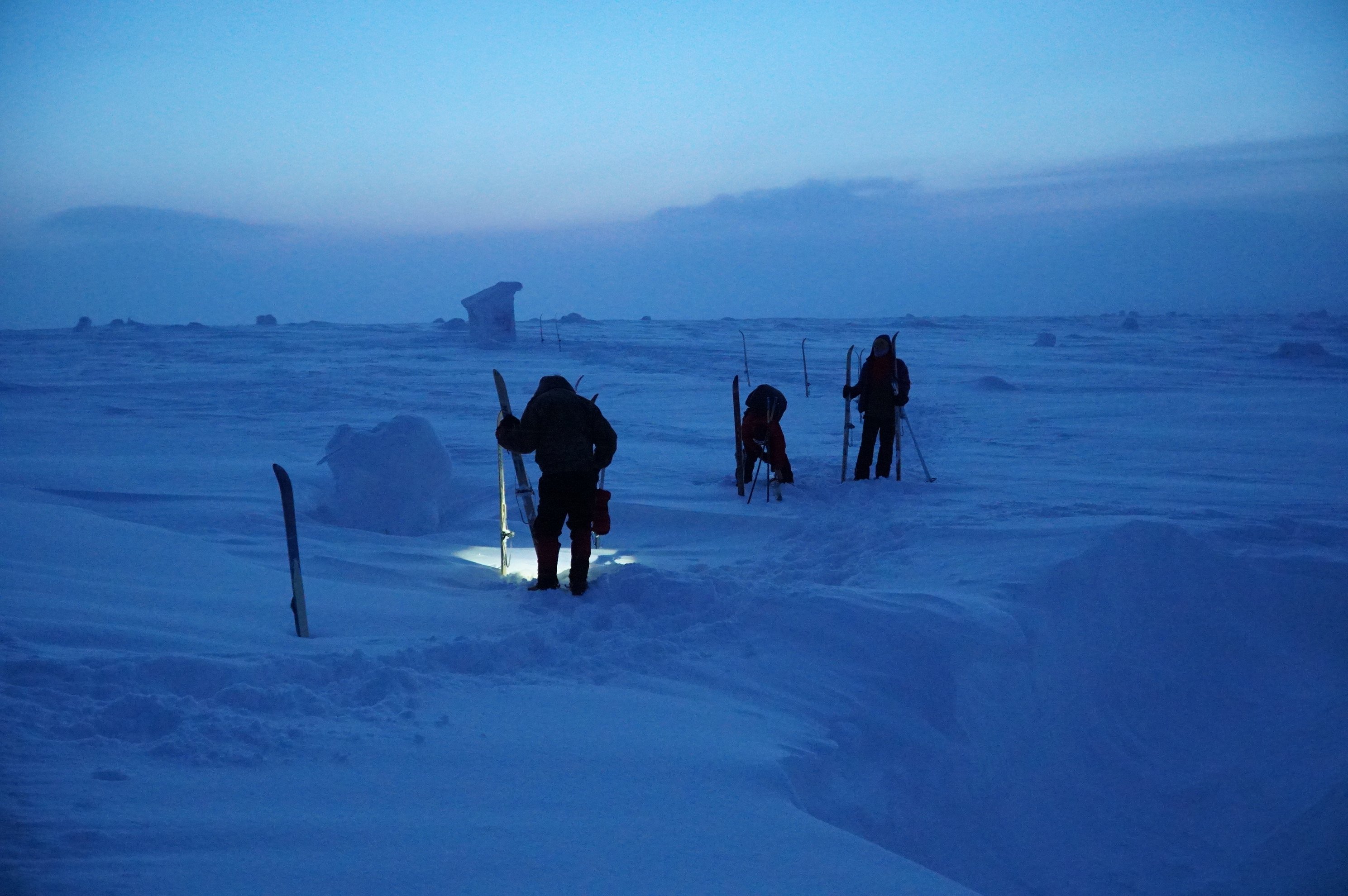 Skiers crossing a snowy field during twilight