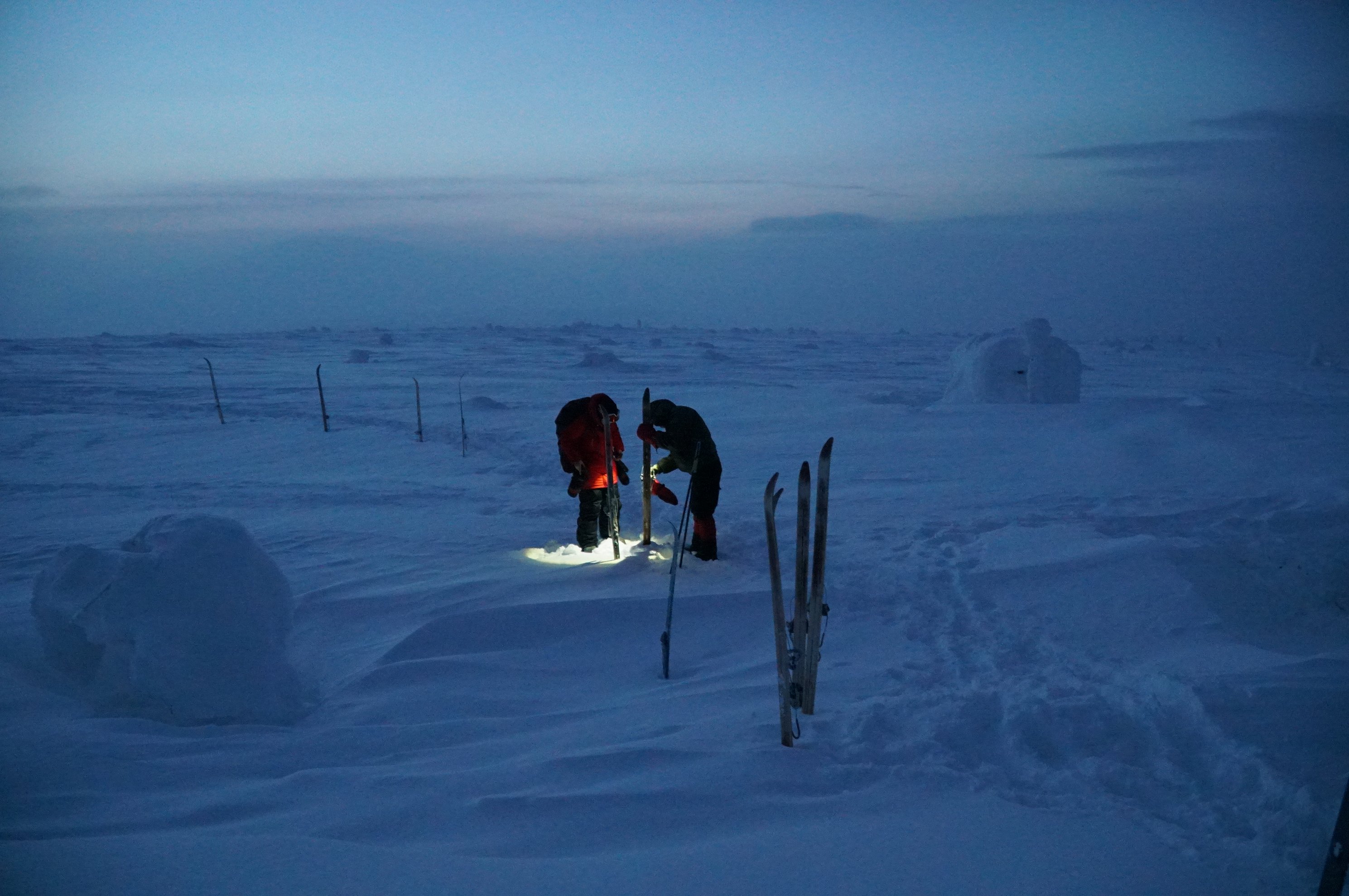 people preparing gear in snow during twilight