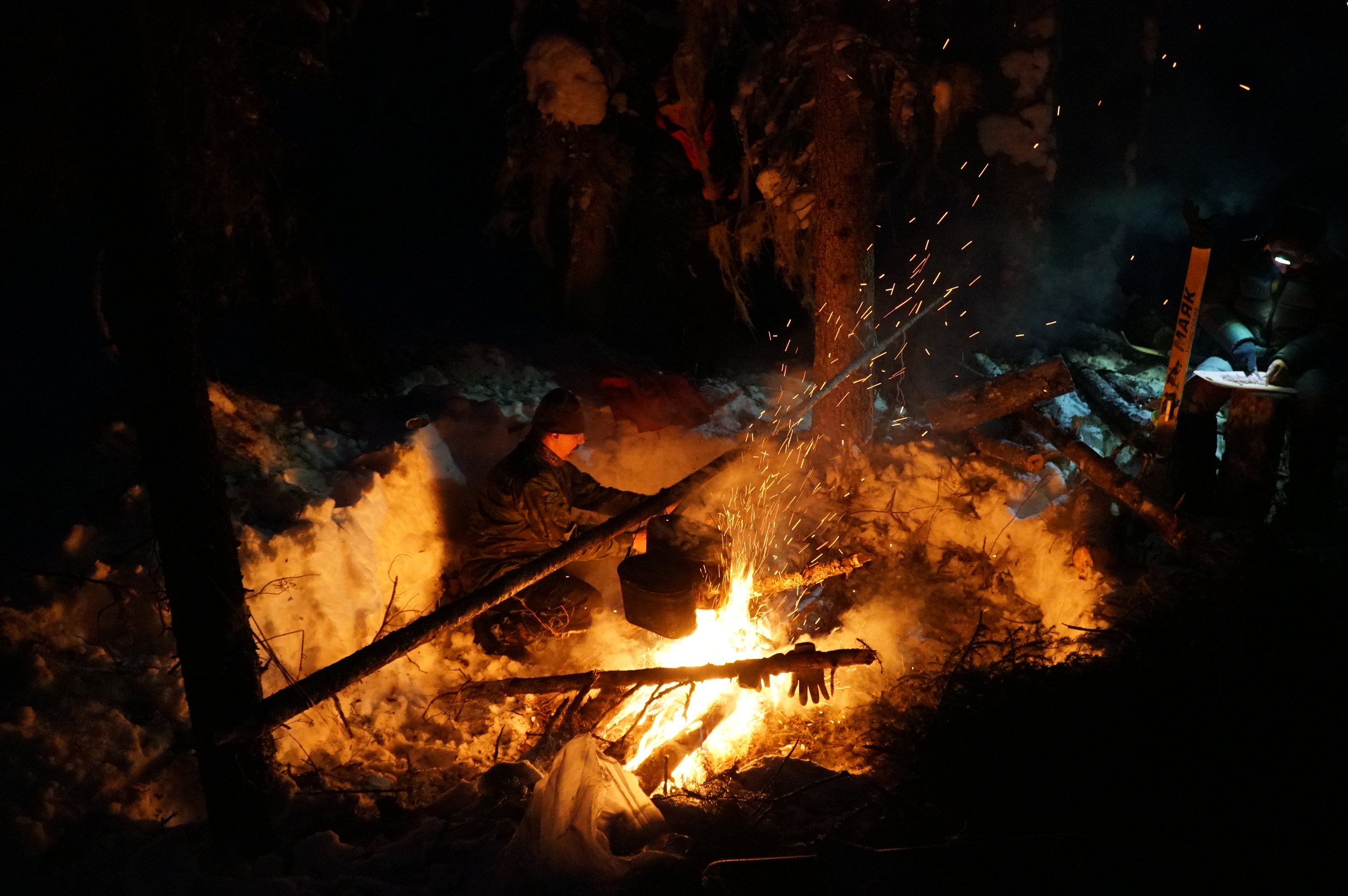 person tending a campfire in the snow at night