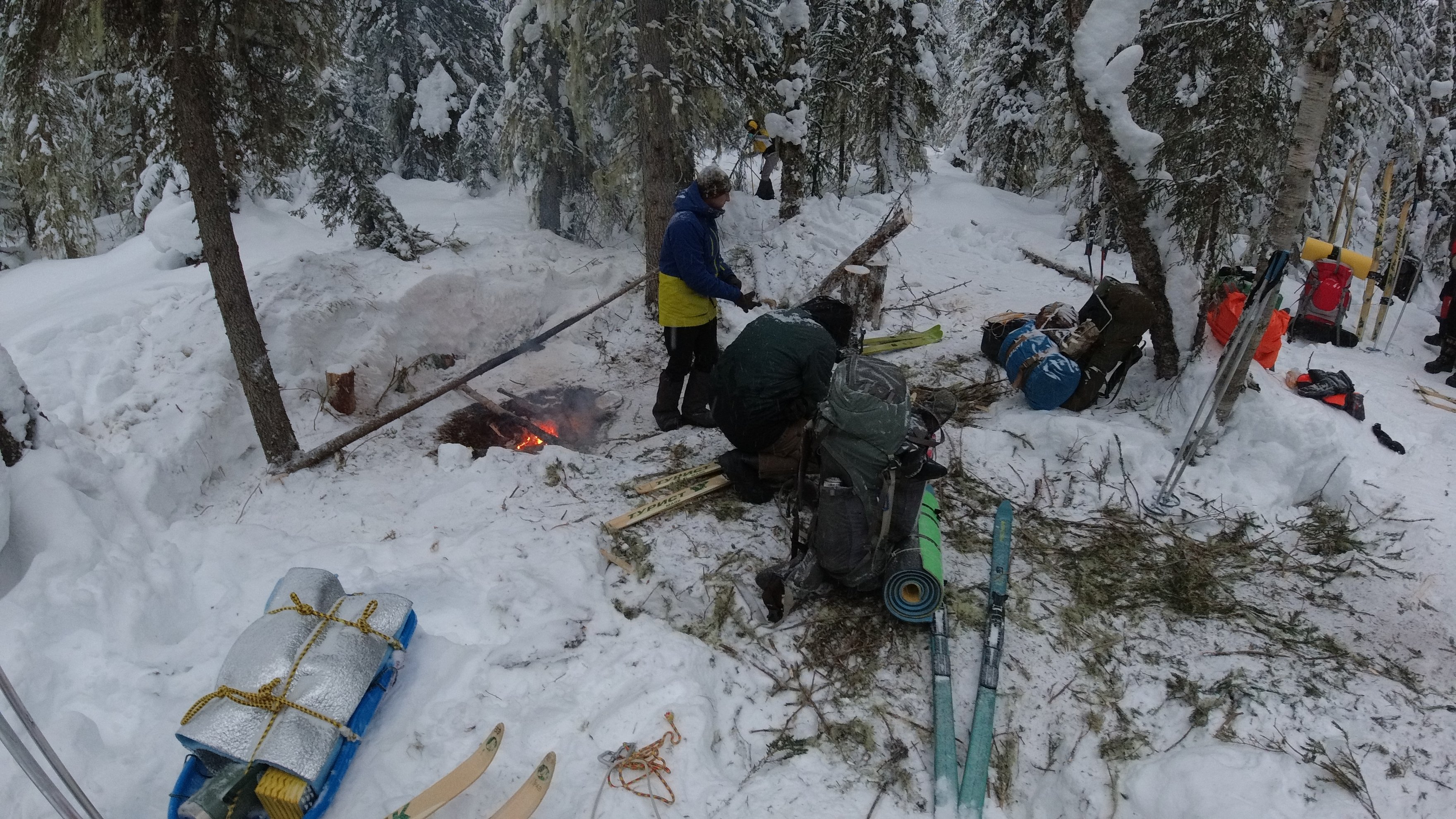 gear and skis near a campfire in snowy woods