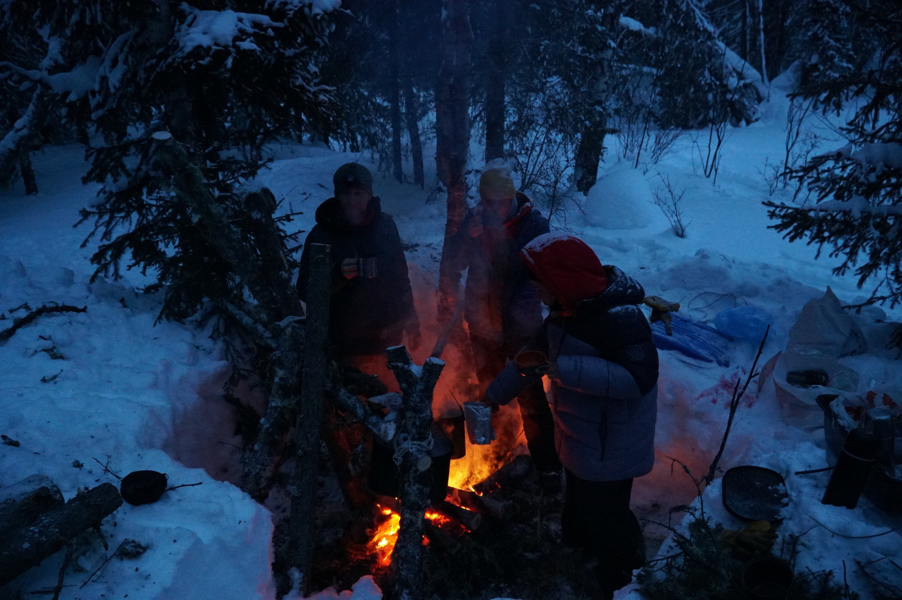 Group gathering around a campfire at night in the snow