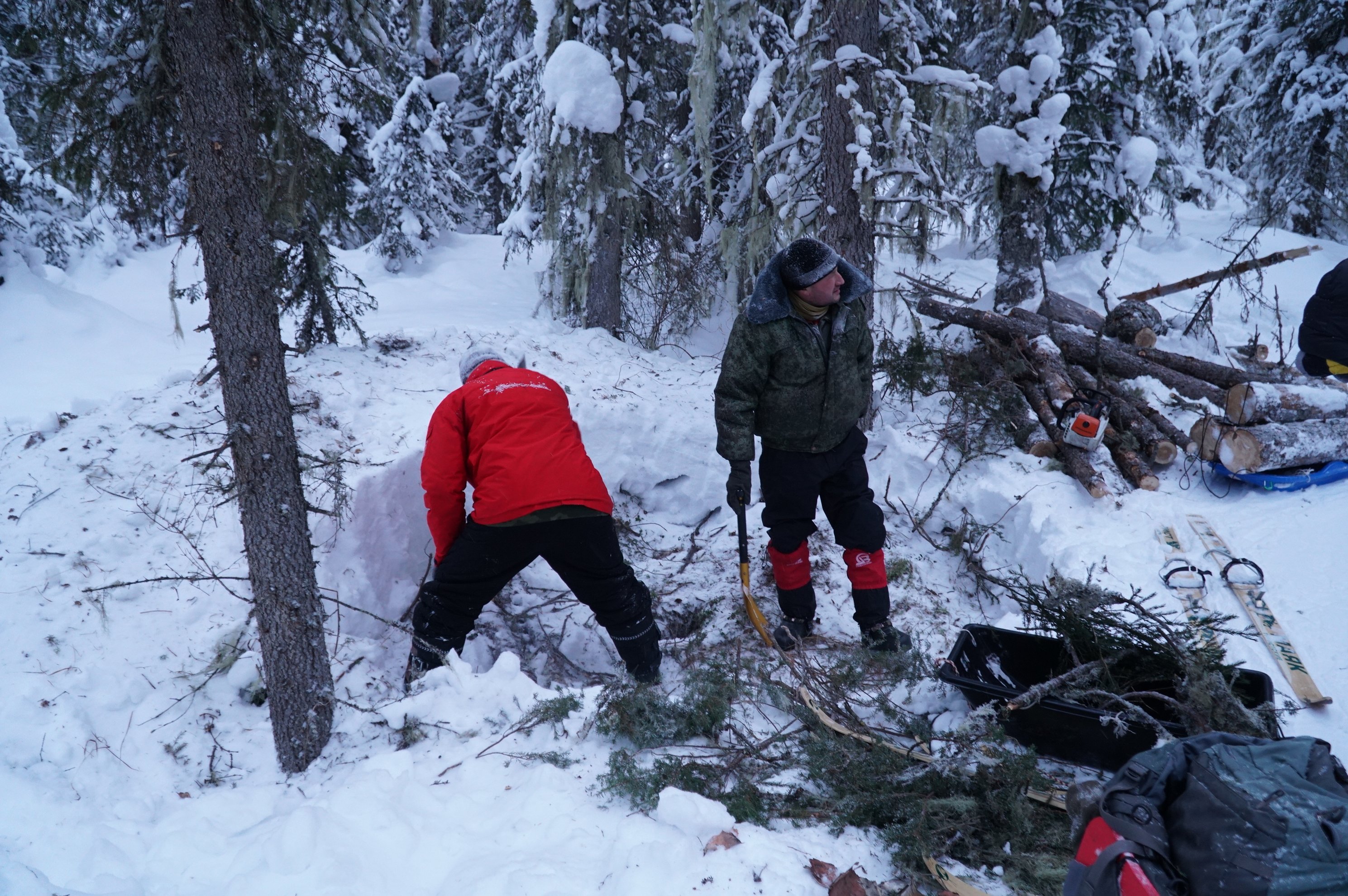 people clearing snow and preparing wood for a campfire