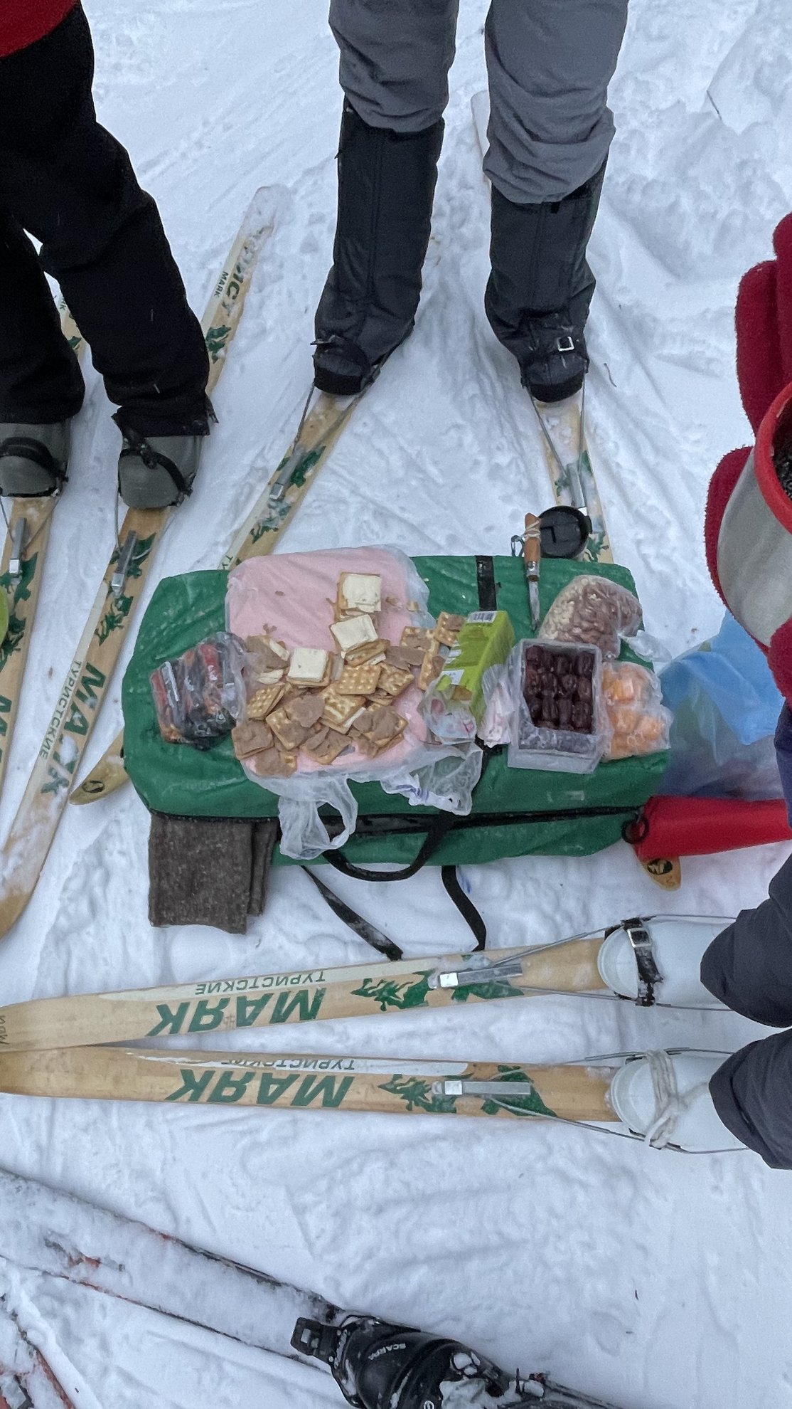 Snacks variados dispostos sobre um tapete verde entre esquis