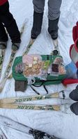 Assorted food snacks laid out on a green mat between skis