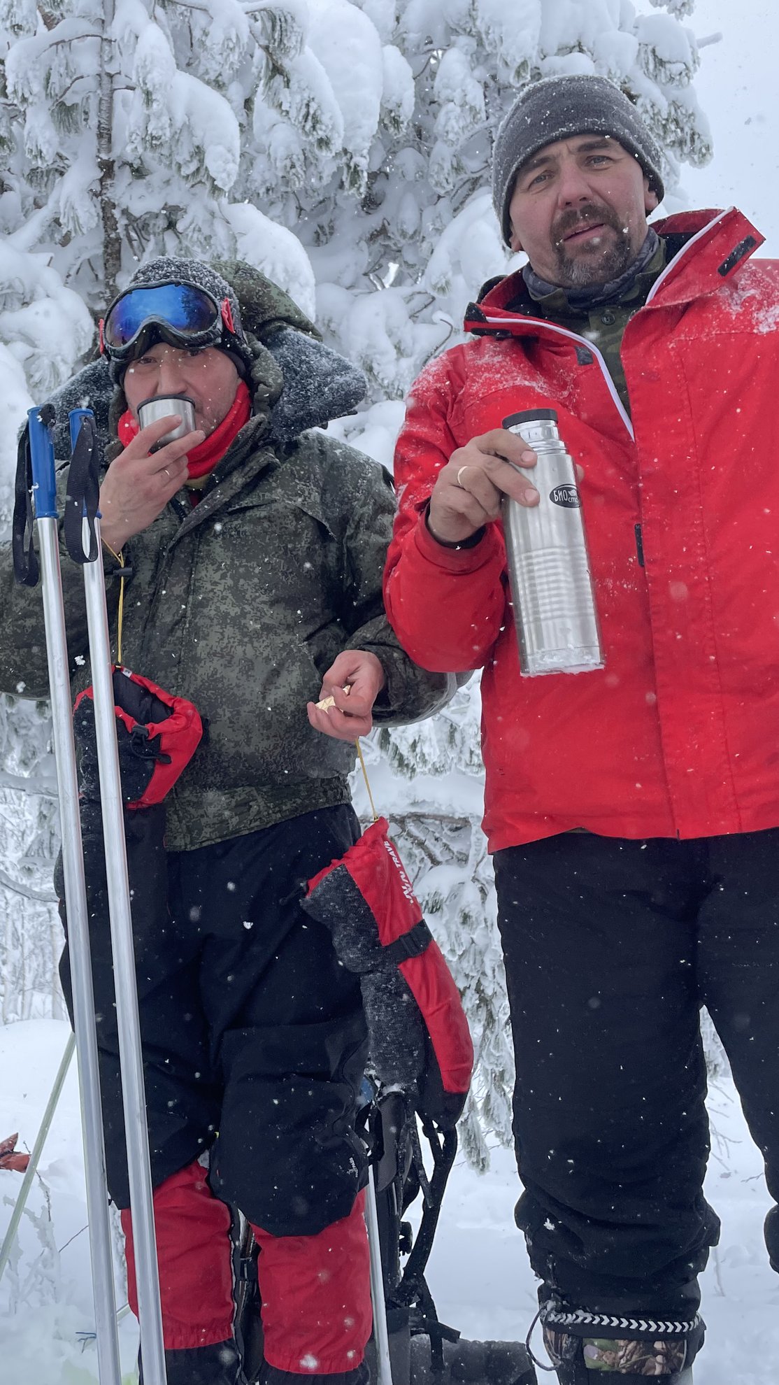 Duas pessoas a segurar uma chávena e um termo na neve