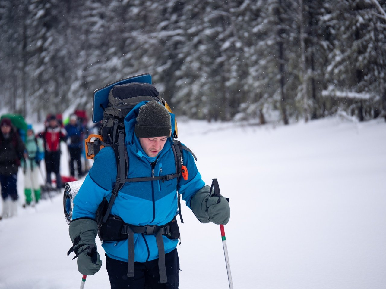 Guide skiing through snow with a large backpack and poles