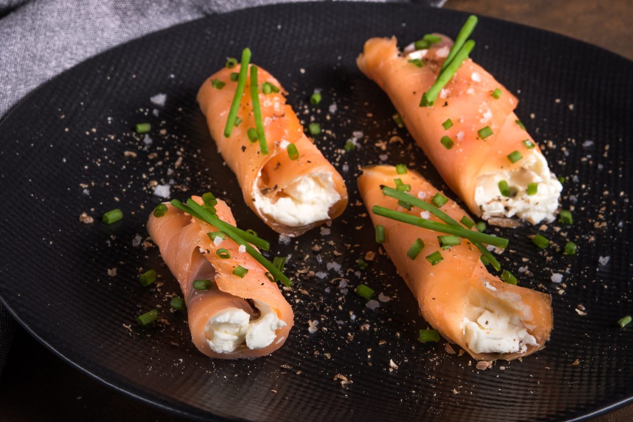 Four salmon rolls on a black plate from a high angle.