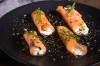 Four salmon rolls on a black plate from a high angle.