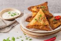 Close up of samosas on parchment paper with side dip.