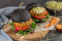 Two burgers on a wooden board with side dipping sauce