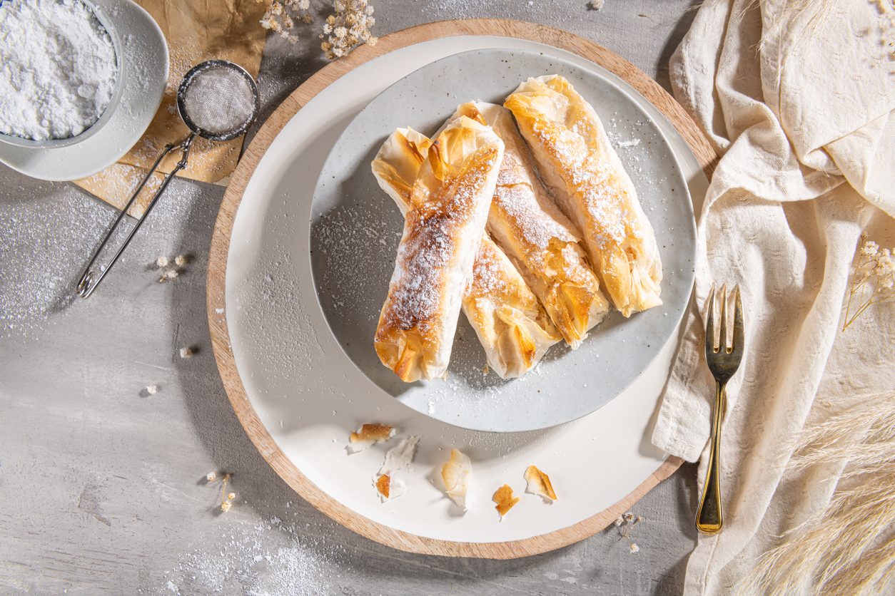 Three pastries on a grey plate with a side of icing sugar