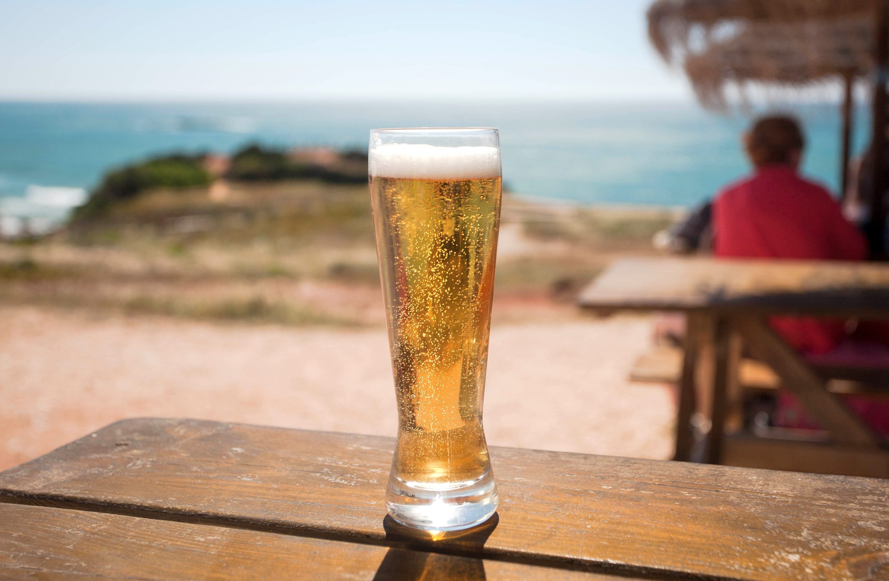 copo de cerveja numa mesa de madeira com vista para a costa