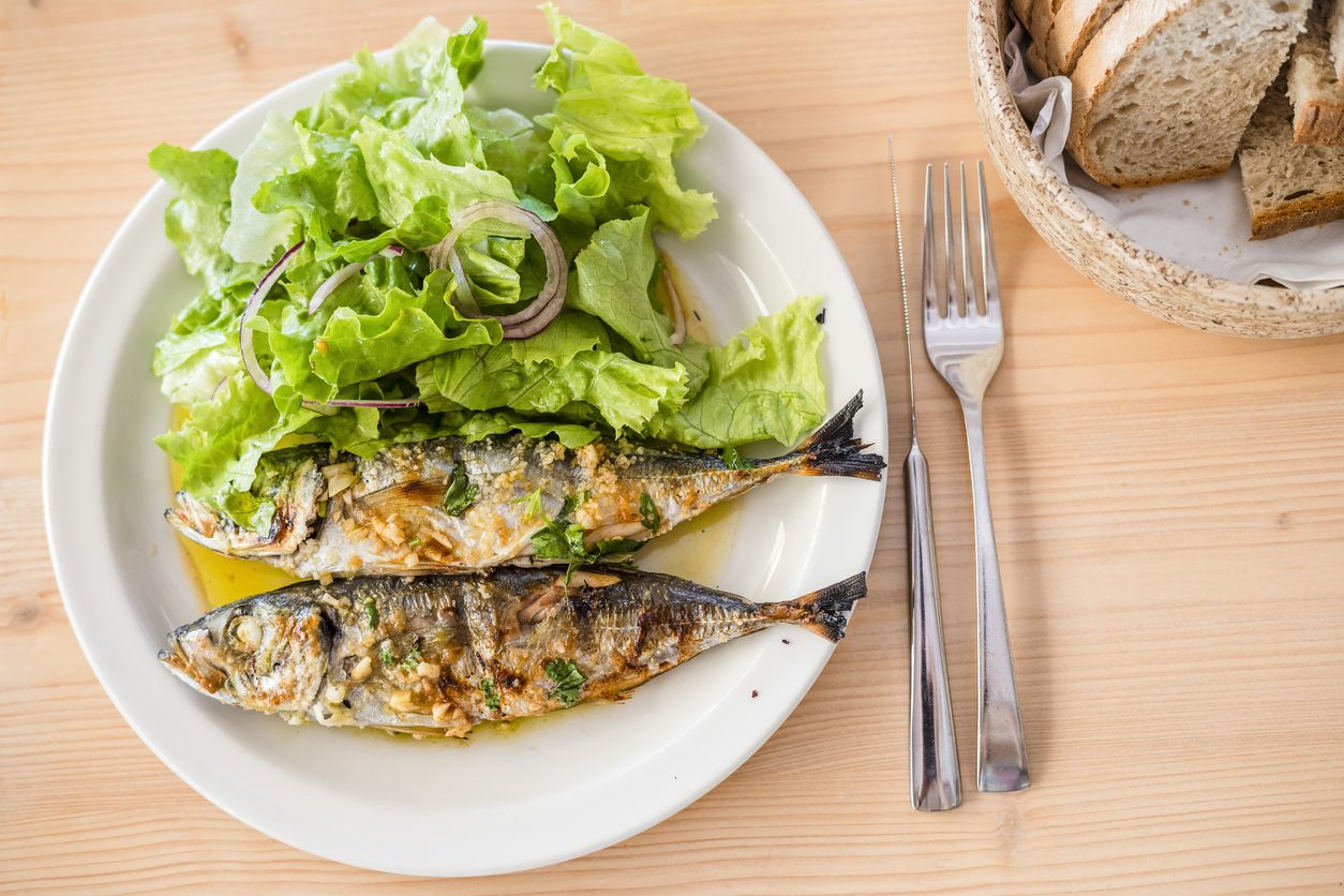 Top-down view of sardines and salad with cutlery and bread.