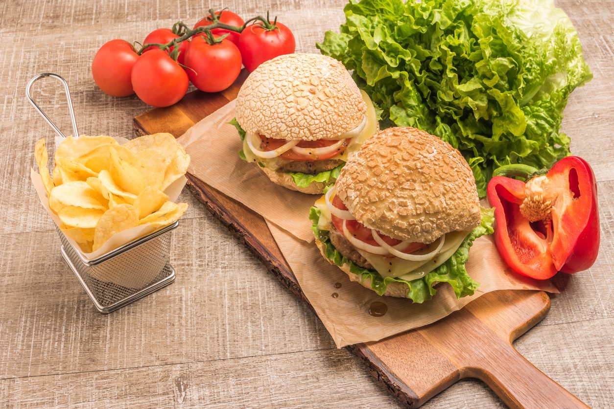 Two burgers and crisps on a board with fresh vegetables
