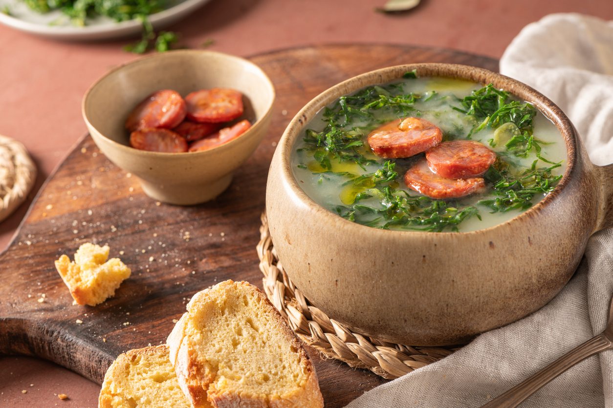 Bowl of soup with chouriço slices and broa bread slices.