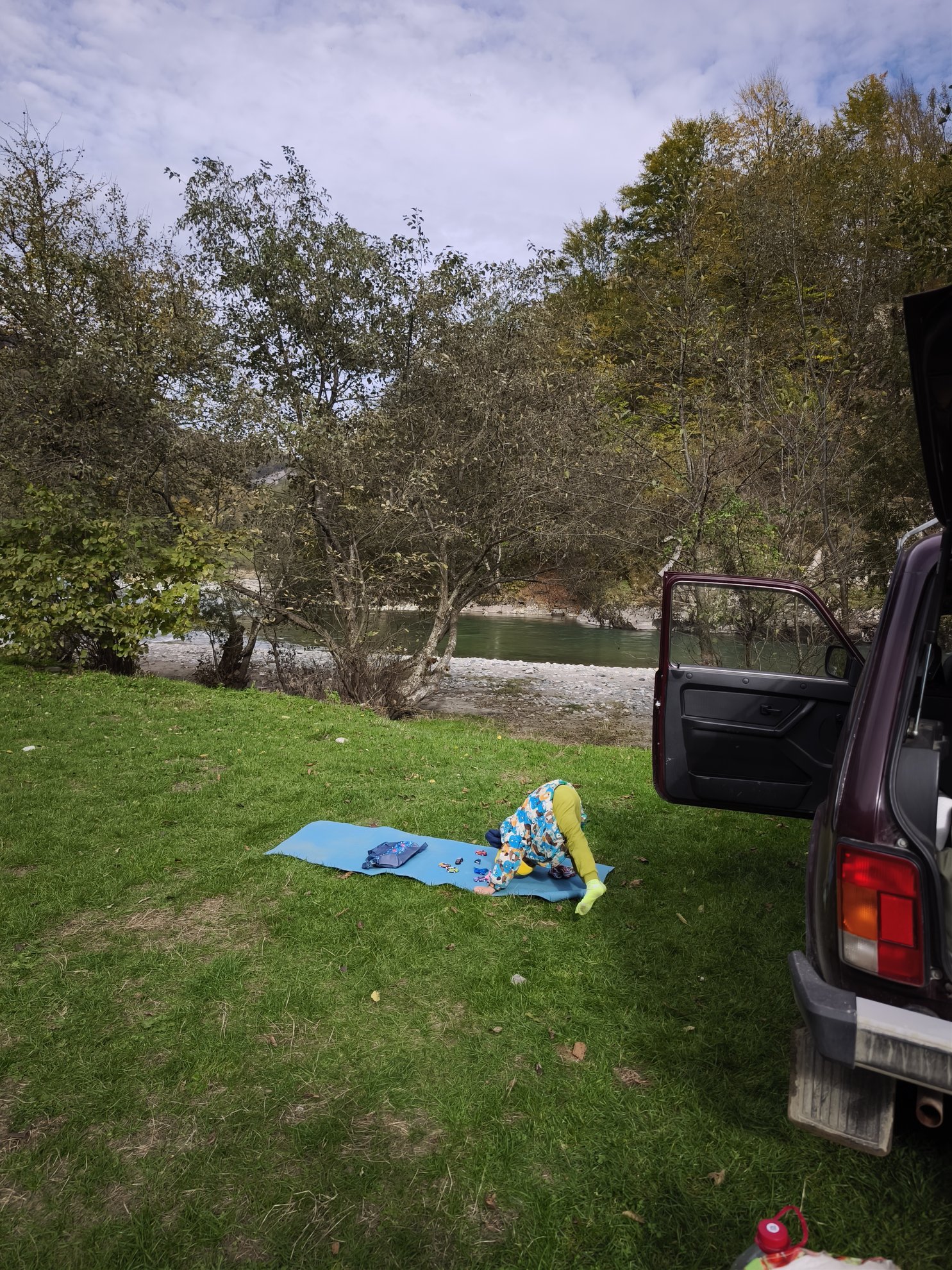 grassy riverbank with a car and a blue mat